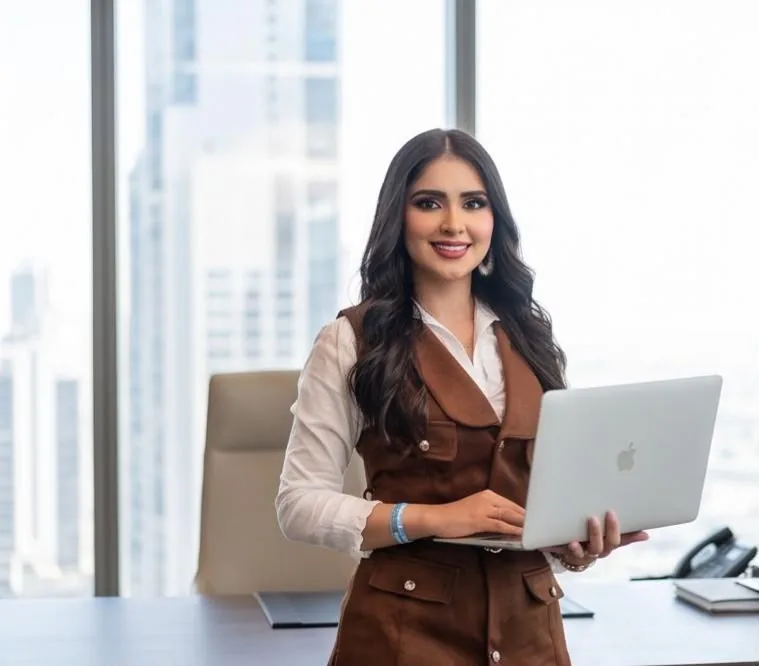 Jeinny García de pie con un portátil frente a ventanales con vista a rascacielos, imagen de Imperio Digital Academy